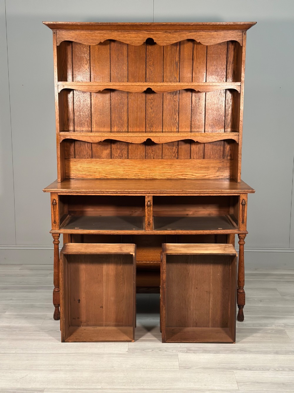 An antique oak Welsh dresser featuring a three-tier open plate rack above two moulded drawers with brass handles and a lower open potboard shelf supported by turned front legs. View VI