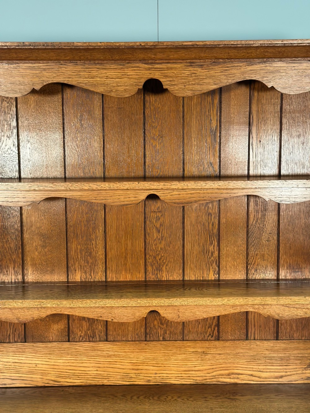 An antique oak Welsh dresser featuring a three-tier open plate rack above two moulded drawers with brass handles and a lower open potboard shelf supported by turned front legs. View VII