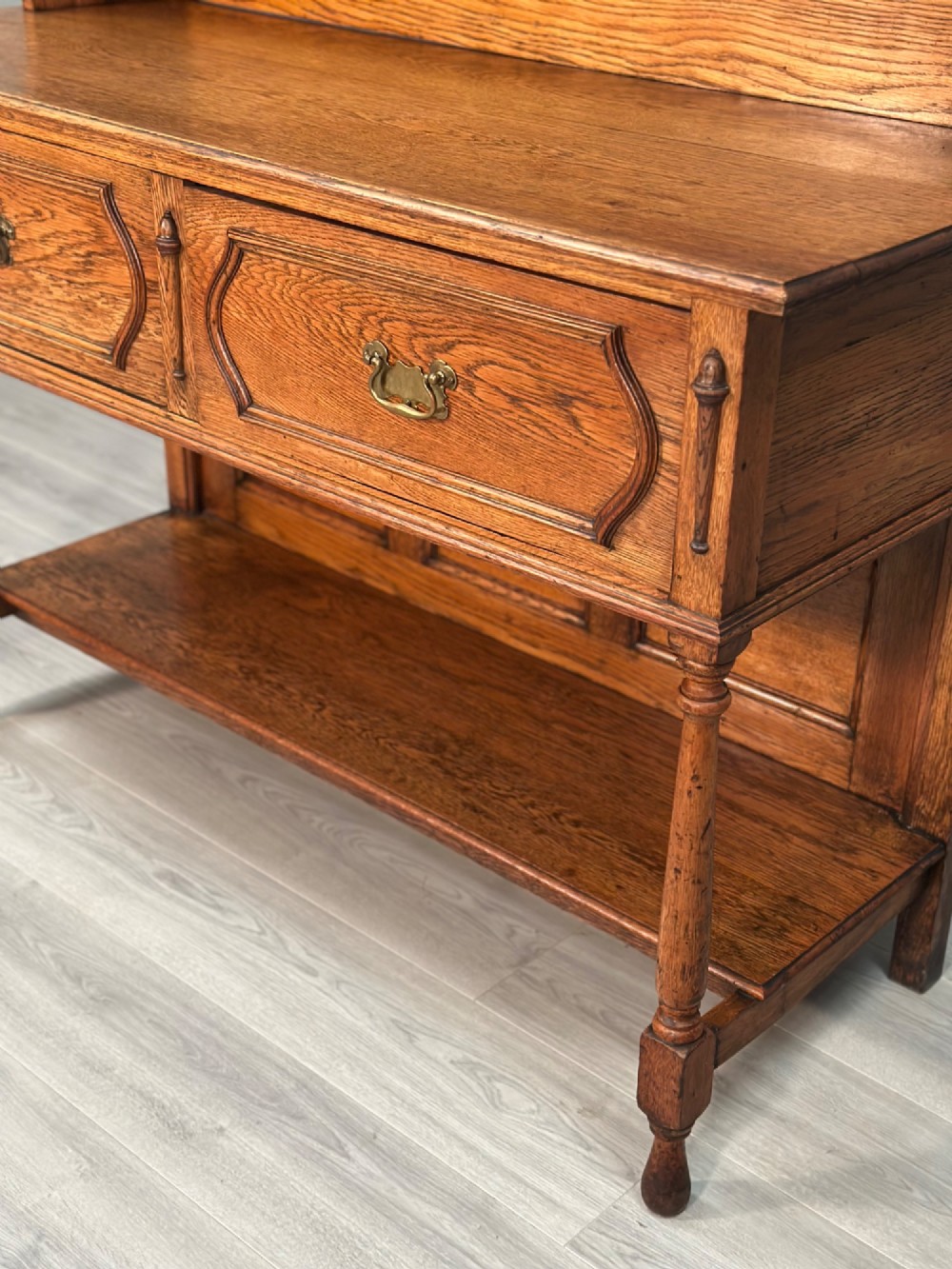 An antique oak Welsh dresser featuring a three-tier open plate rack above two moulded drawers with brass handles and a lower open potboard shelf supported by turned front legs. View VIII
