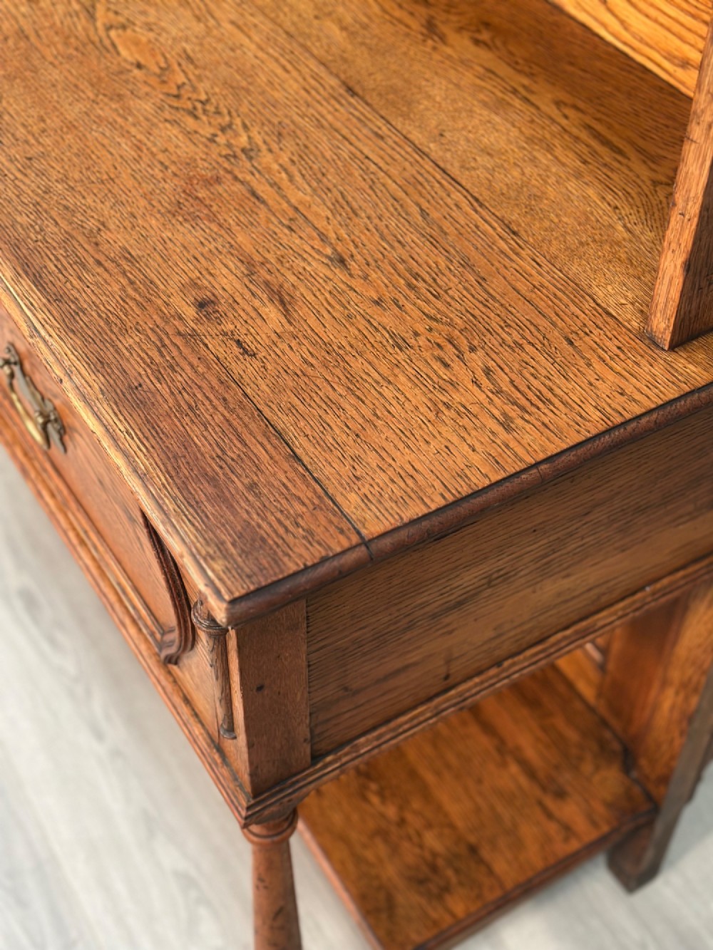 An antique oak Welsh dresser featuring a three-tier open plate rack above two moulded drawers with brass handles and a lower open potboard shelf supported by turned front legs. View IX