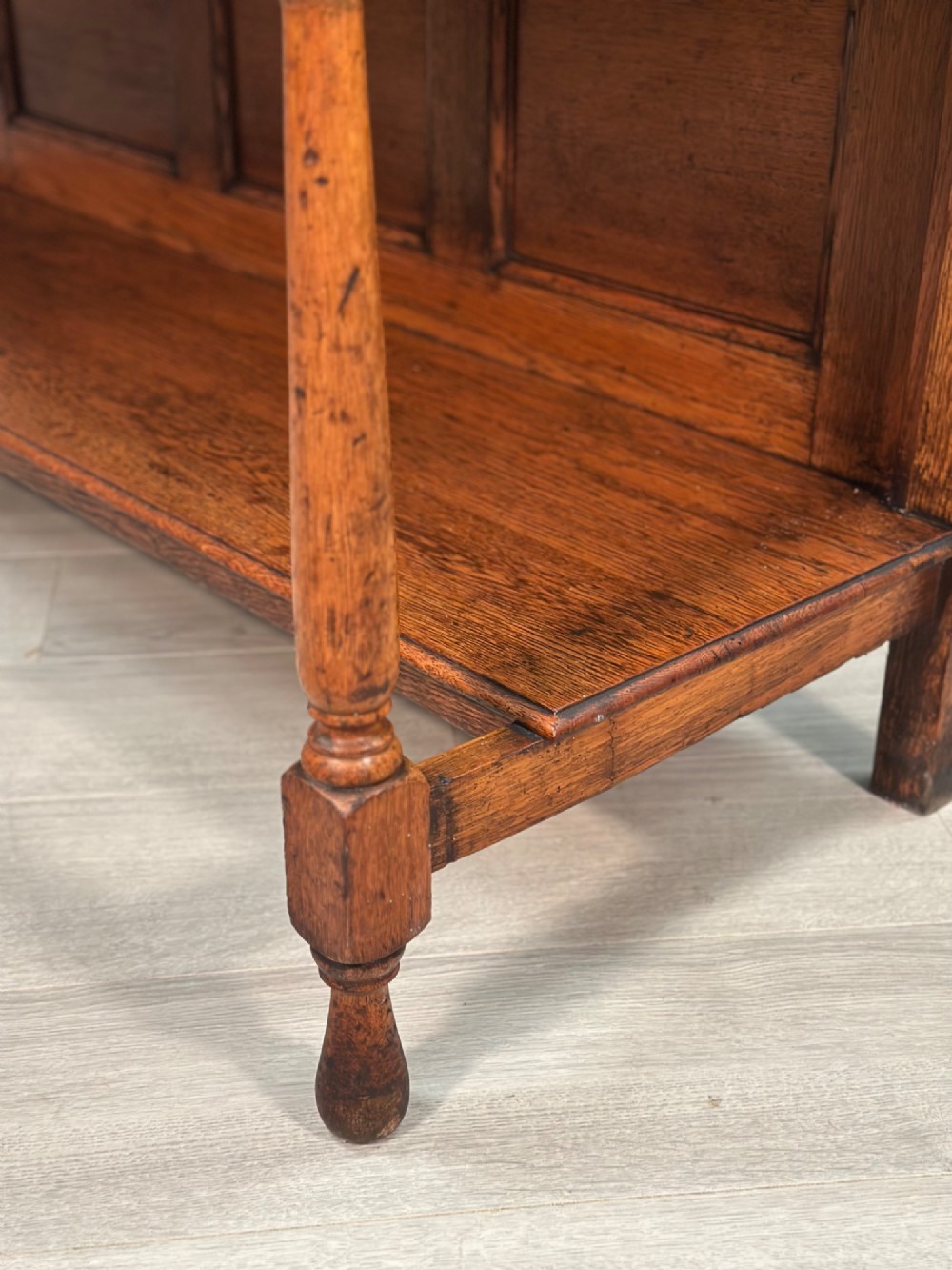 An antique oak Welsh dresser featuring a three-tier open plate rack above two moulded drawers with brass handles and a lower open potboard shelf supported by turned front legs. View XIII