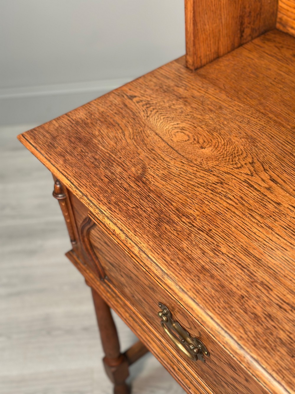An antique oak Welsh dresser featuring a three-tier open plate rack above two moulded drawers with brass handles and a lower open potboard shelf supported by turned front legs. View XIV