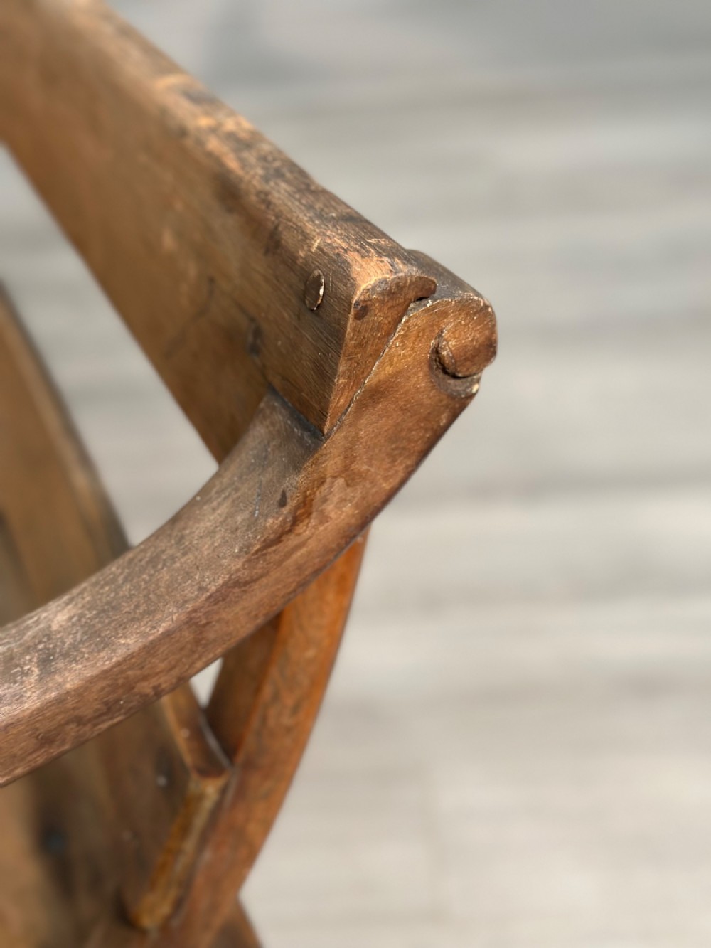 A long antique wooden rocking settle featuring open back slats, curved scroll armrests, and a solid plank seat resting on wooden rocking runners. View XII