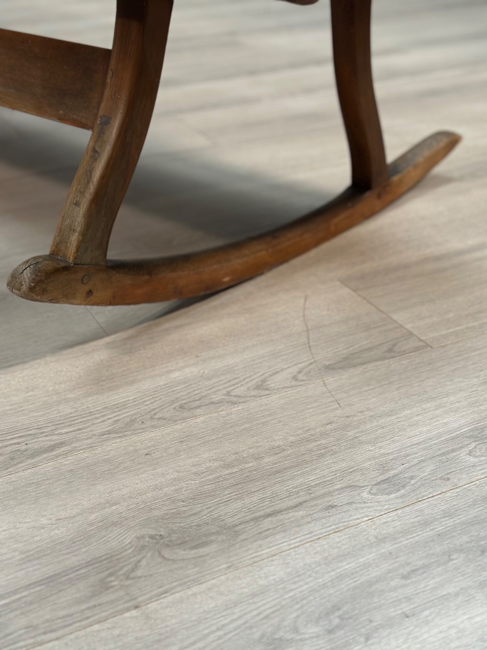 A long antique wooden rocking settle featuring open back slats, curved scroll armrests, and a solid plank seat resting on wooden rocking runners. View XIII