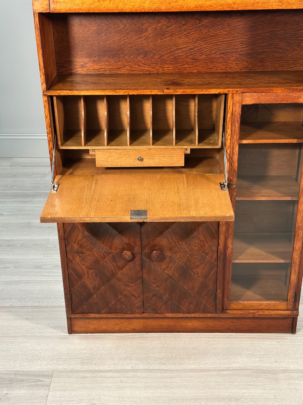 An Art Deco oak bureau bookcase featuring an open top shelf, drop-down writing flap, a glazed side cabinet, and lower cupboards with geometric diamond veneer. View III