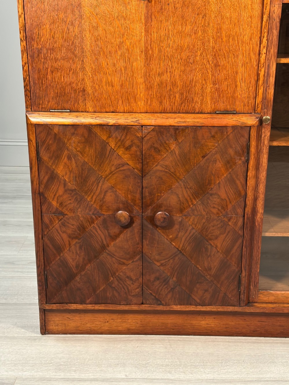 An Art Deco oak bureau bookcase featuring an open top shelf, drop-down writing flap, a glazed side cabinet, and lower cupboards with geometric diamond veneer. View V