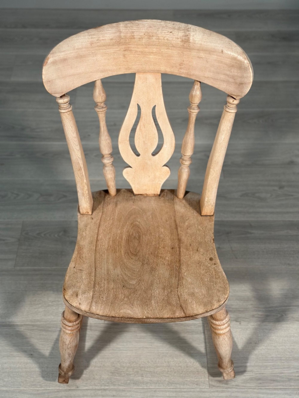 A small antique pale wood rocking chair featuring turned spindles, a pierced central back splat, and curved wooden rockers. View III