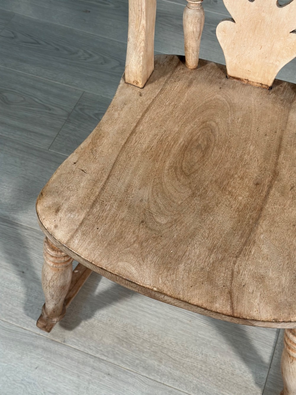 A small antique pale wood rocking chair featuring turned spindles, a pierced central back splat, and curved wooden rockers. View IV