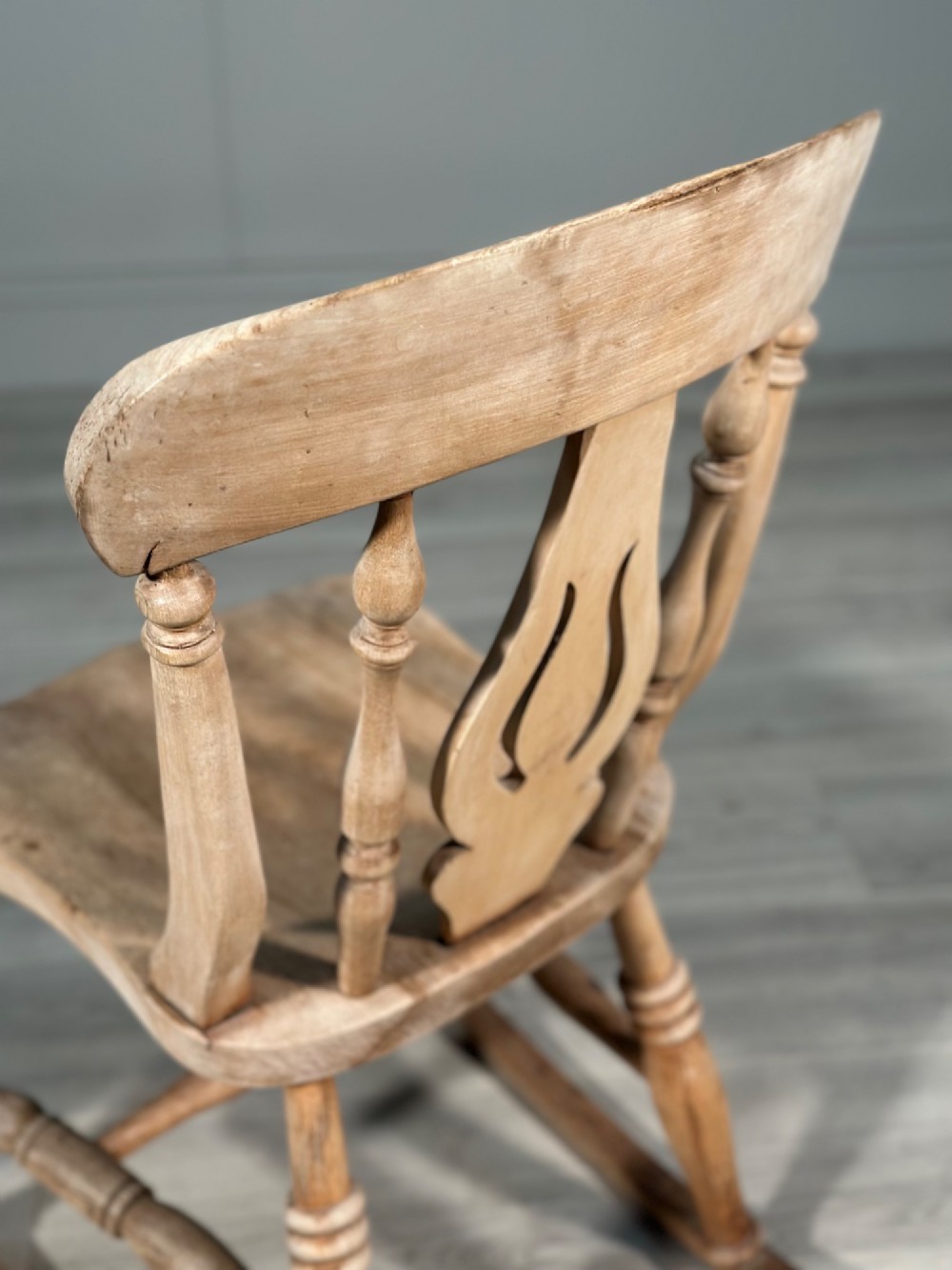 A small antique pale wood rocking chair featuring turned spindles, a pierced central back splat, and curved wooden rockers. View VII
