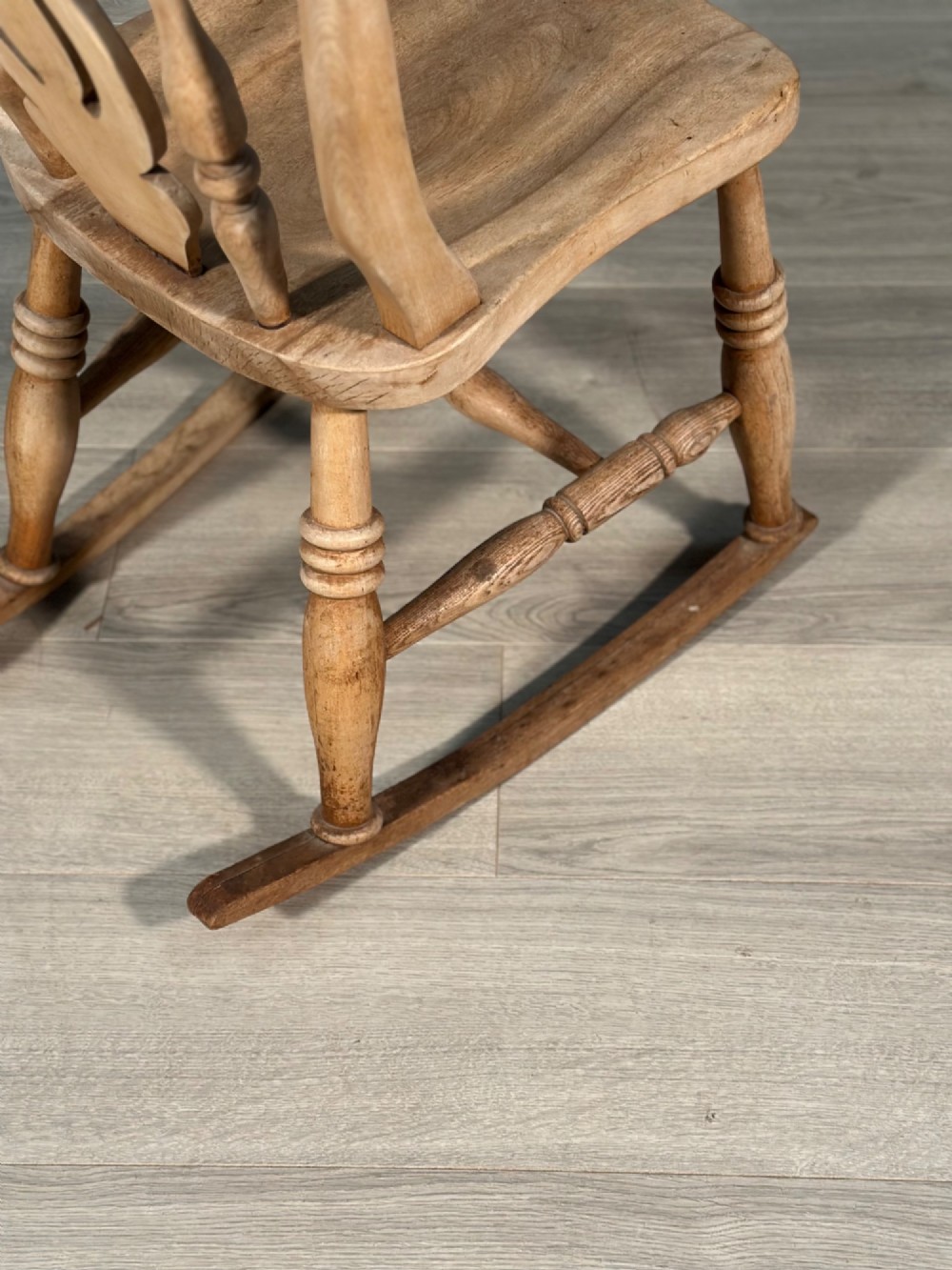 A small antique pale wood rocking chair featuring turned spindles, a pierced central back splat, and curved wooden rockers. View IX