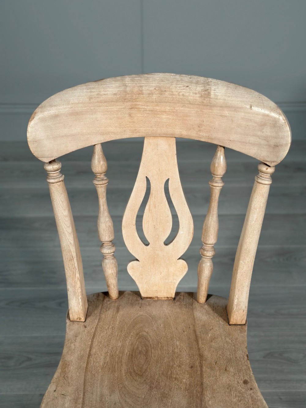 A small antique pale wood rocking chair featuring turned spindles, a pierced central back splat, and curved wooden rockers. View X