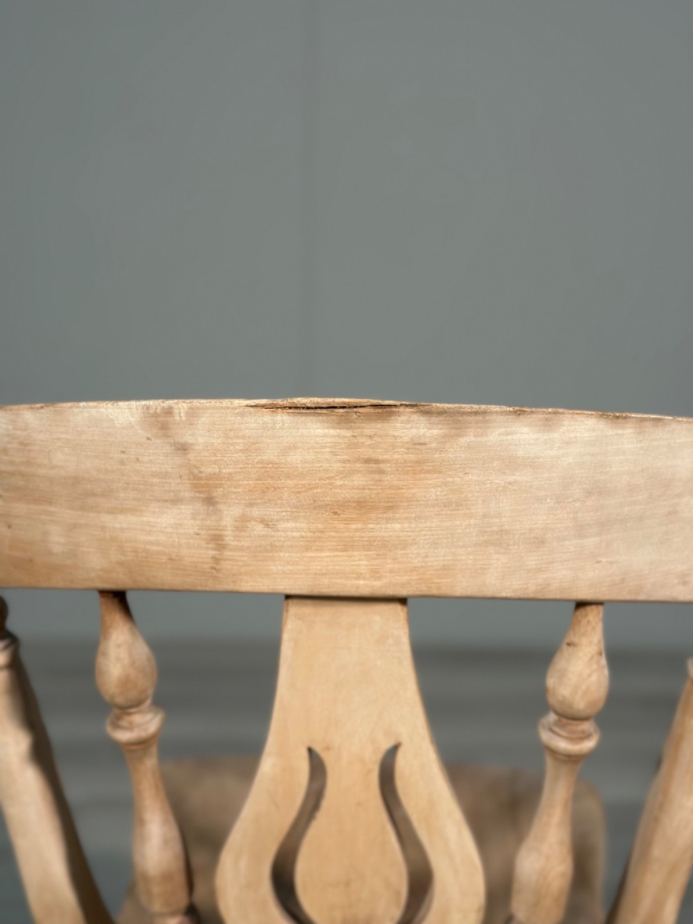A small antique pale wood rocking chair featuring turned spindles, a pierced central back splat, and curved wooden rockers. View XIII