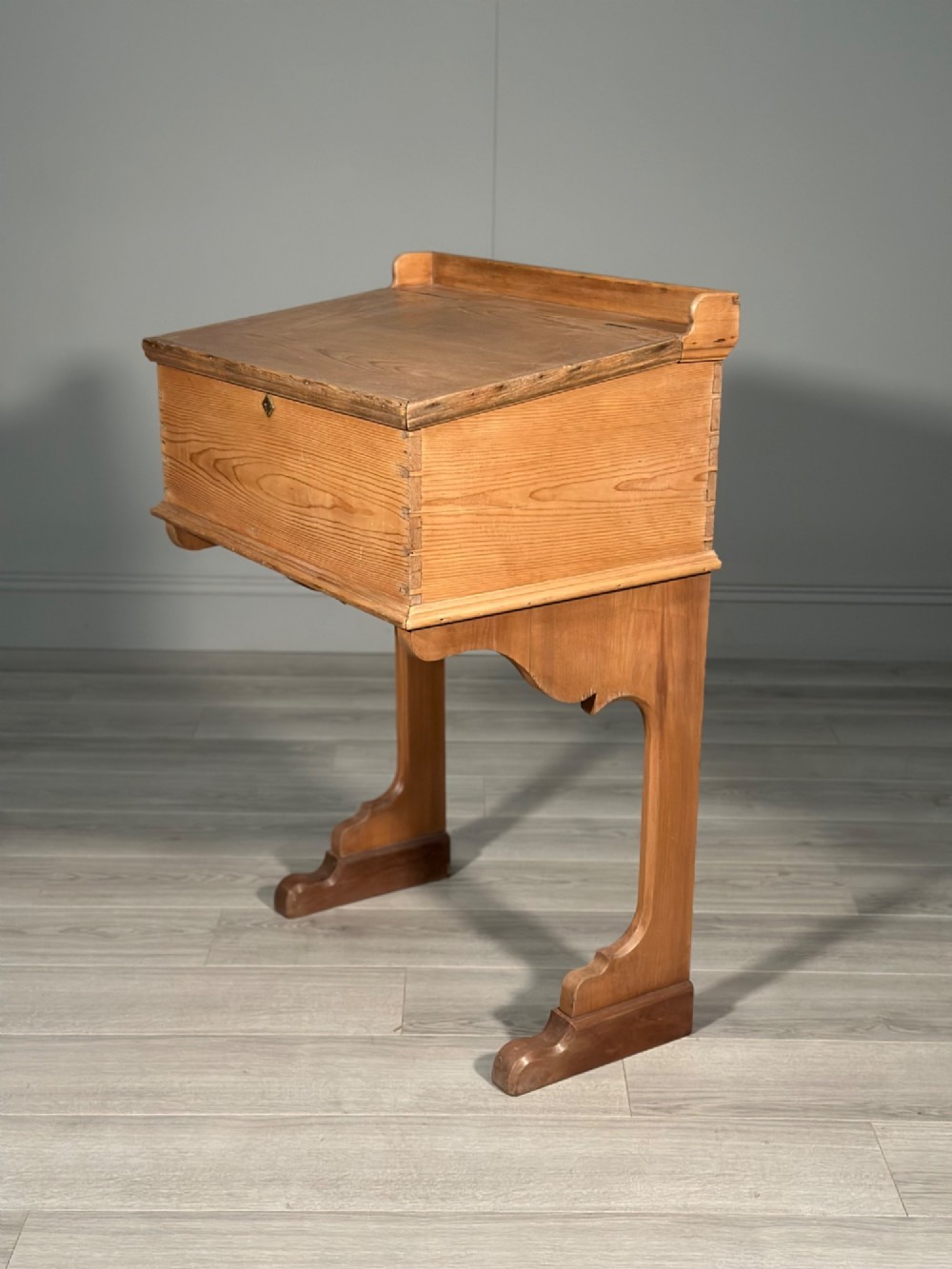 A Victorian pine school desk featuring a slanted hinged lid, dovetail joinery, shaped side supports, and a raised back gallery.