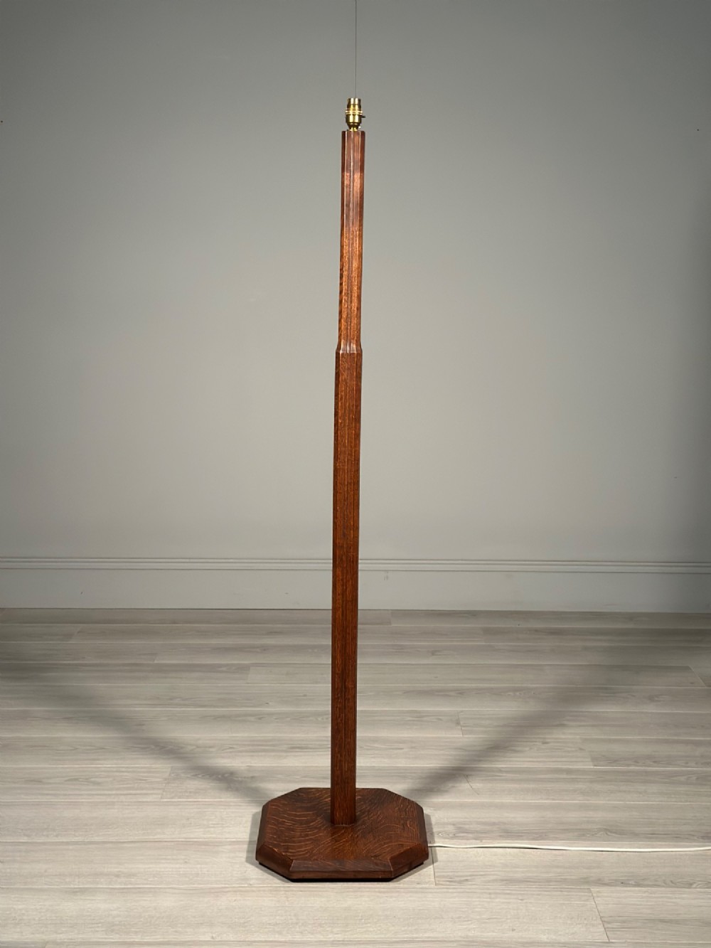 An Arts and Crafts solid oak standard lamp featuring a faceted tapered column on an octagonal base with brass bulb holder. View II