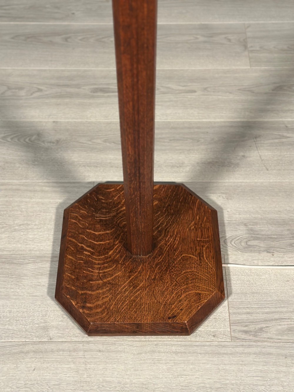 An Arts and Crafts solid oak standard lamp featuring a faceted tapered column on an octagonal base with brass bulb holder. View III
