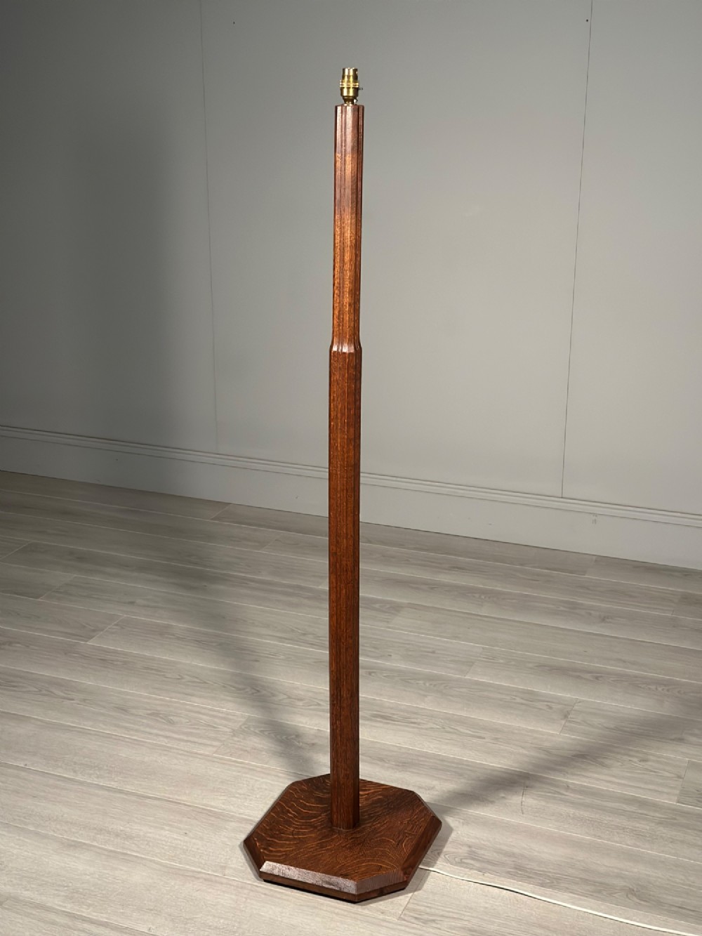An Arts and Crafts solid oak standard lamp featuring a faceted tapered column on an octagonal base with brass bulb holder. View V