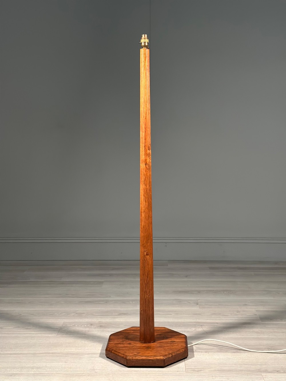 A tall Arts and Crafts solid oak standard lamp featuring a faceted stem mounted on an octagonal base with a brass light socket.