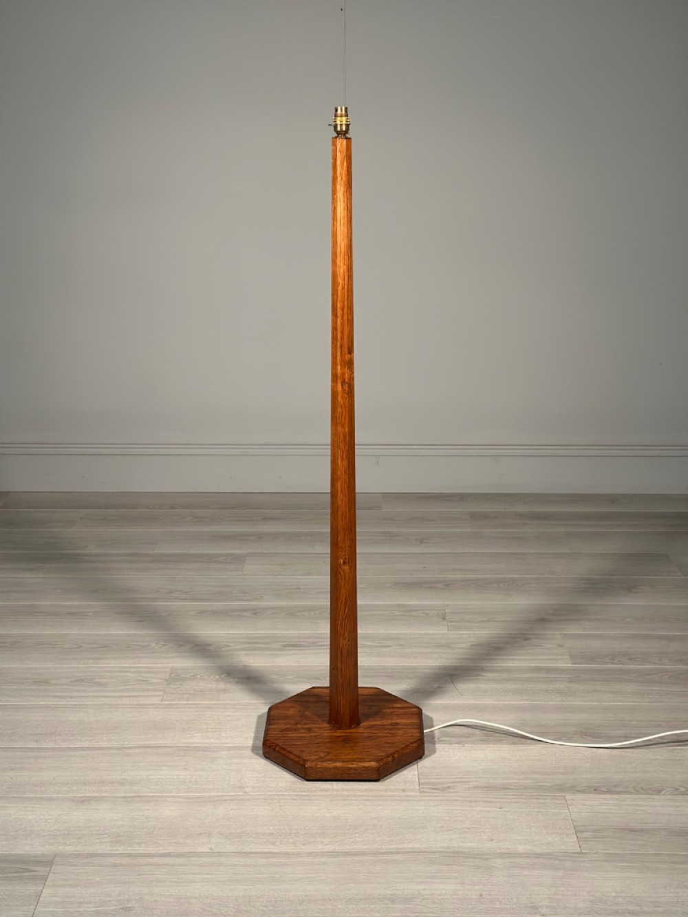 A tall Arts and Crafts solid oak standard lamp featuring a faceted stem mounted on an octagonal base with a brass light socket. View II