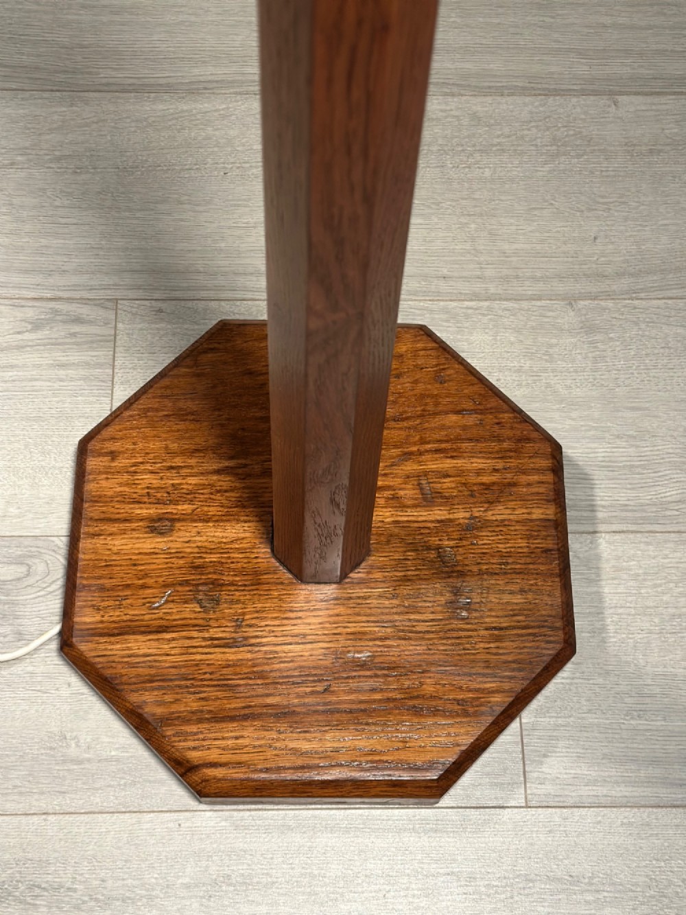 A tall Arts and Crafts solid oak standard lamp featuring a faceted stem mounted on an octagonal base with a brass light socket. View V