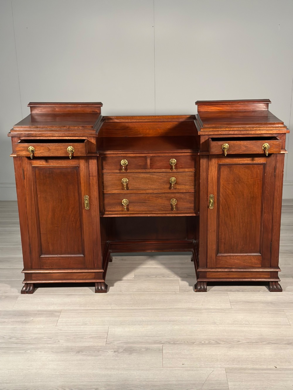 An Edwardian mahogany pedestal sideboard featuring two outer pedestal cupboards, central drawers, and brass drop handles. View IV