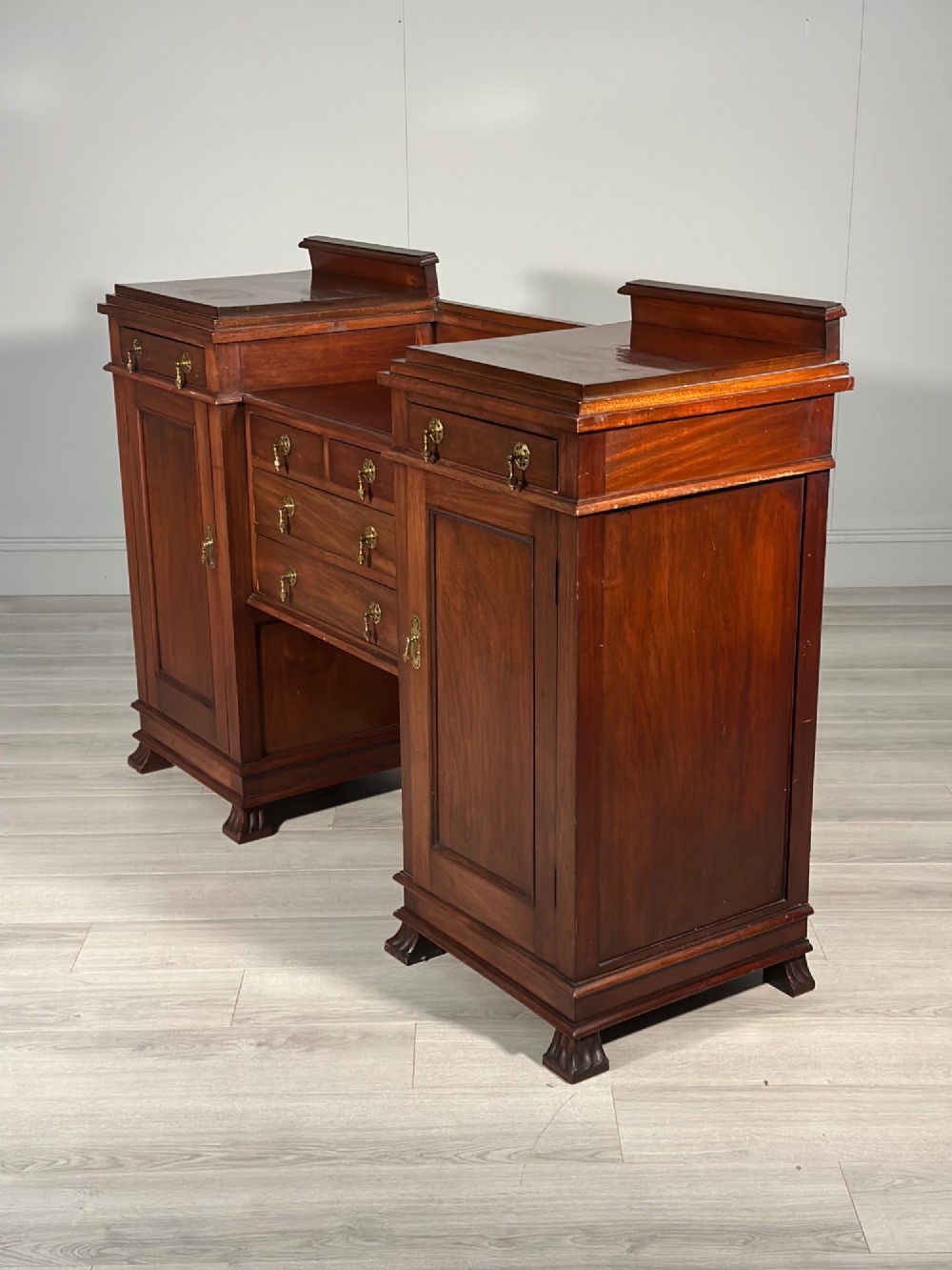 An Edwardian mahogany pedestal sideboard featuring two outer pedestal cupboards, central drawers, and brass drop handles. View VI