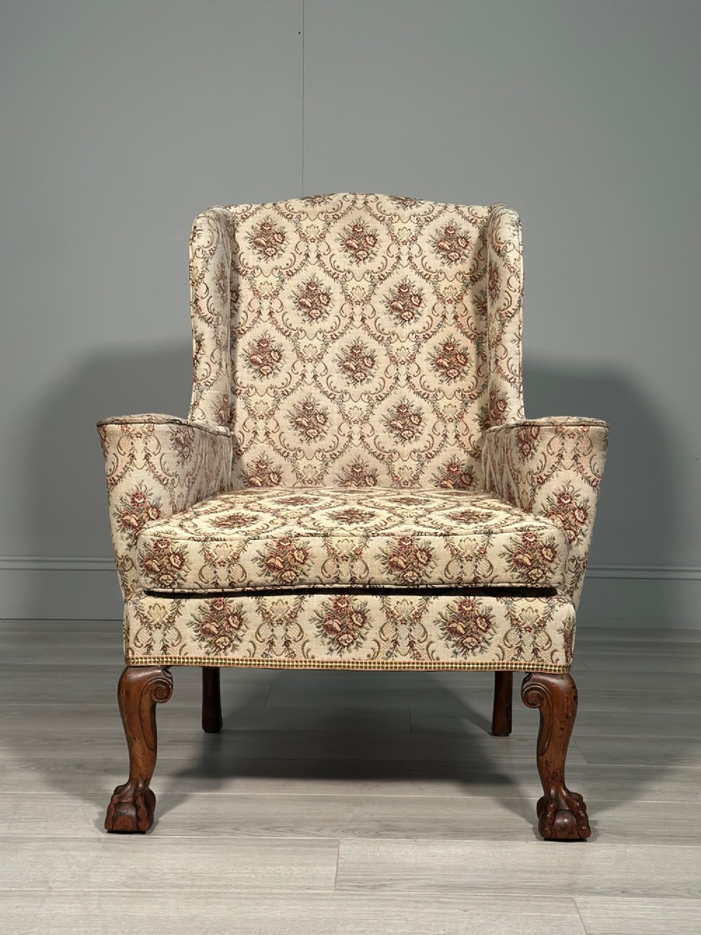 An Edwardian wingback armchair upholstered in cream floral patterned fabric with carved mahogany cabriole legs and ball-and-claw feet.