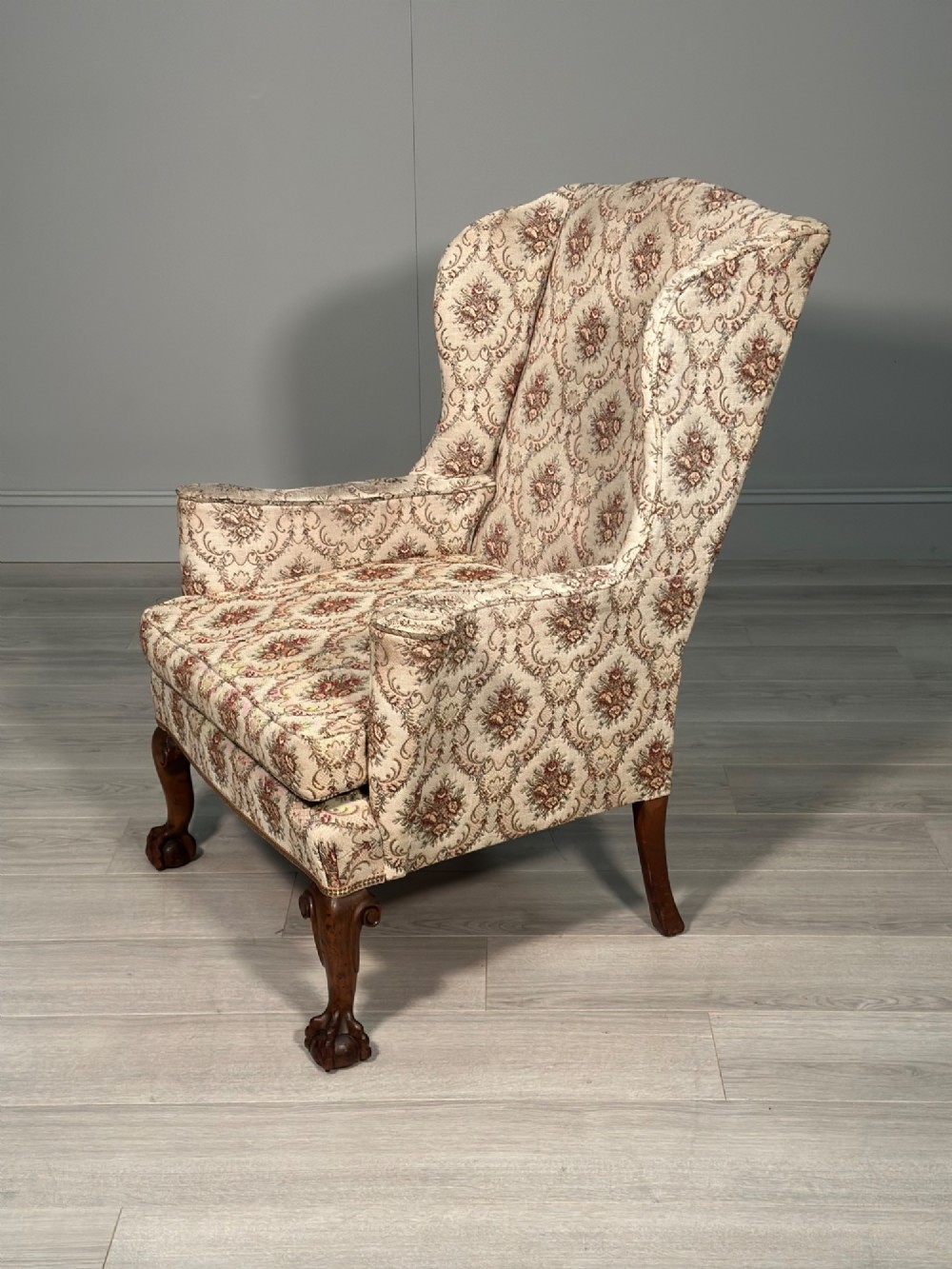 An Edwardian wingback armchair upholstered in cream floral patterned fabric with carved mahogany cabriole legs and ball-and-claw feet. View V