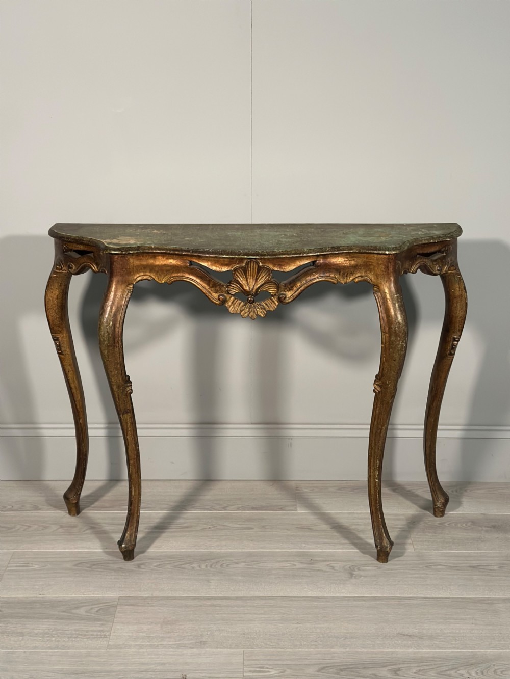 A Rococo style carved giltwood console table featuring cabriole legs, central shell motif, serpentine apron, and a dark marble top.