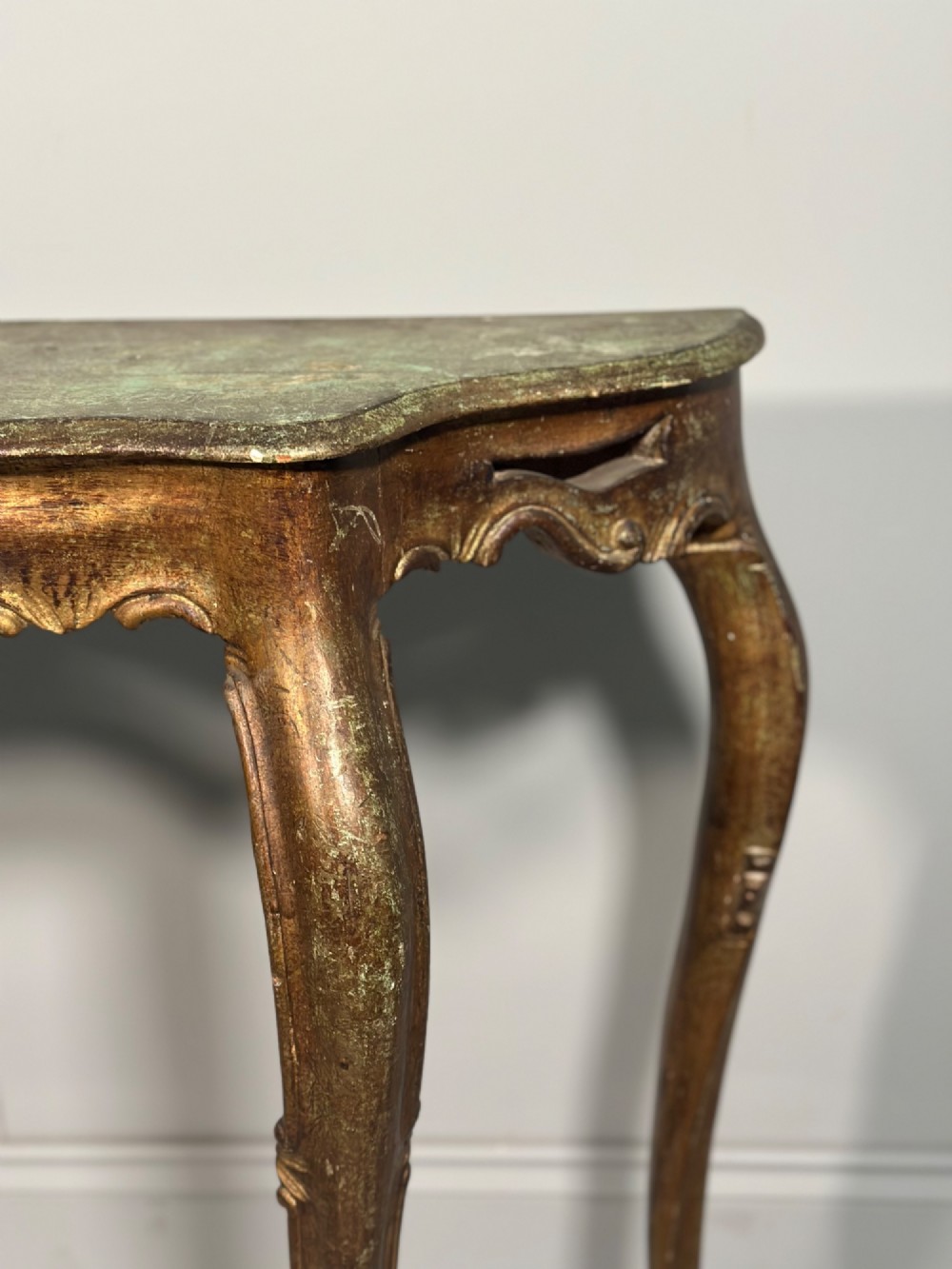 A Rococo style carved giltwood console table featuring cabriole legs, central shell motif, serpentine apron, and a dark marble top. View IX