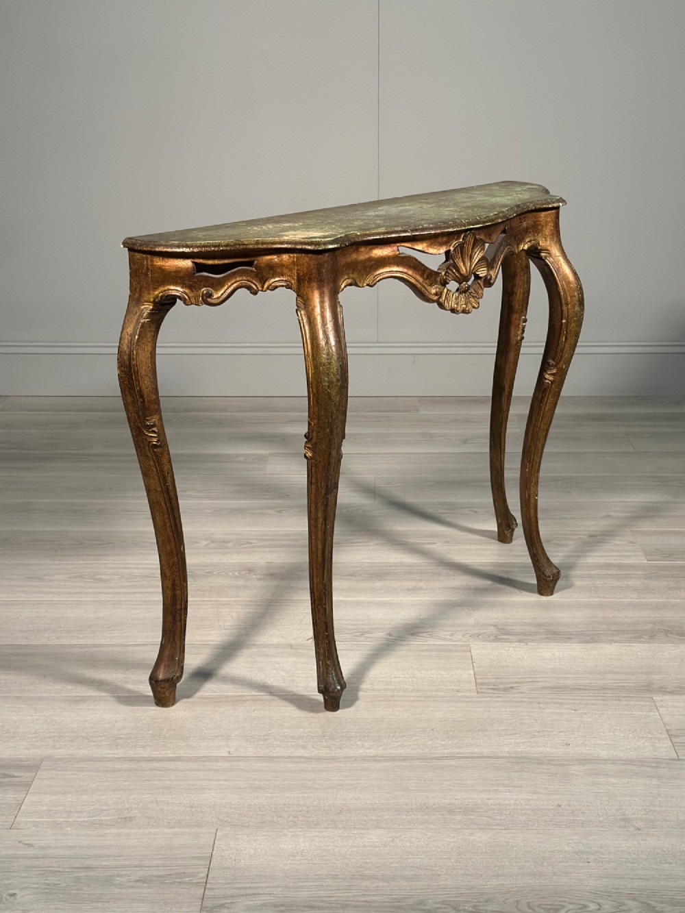 A Rococo style carved giltwood console table featuring cabriole legs, central shell motif, serpentine apron, and a dark marble top. View X