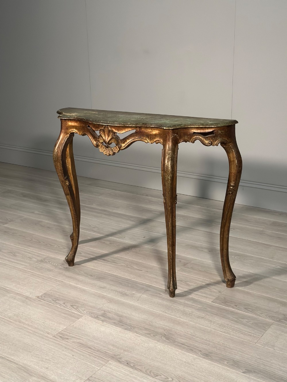 A Rococo style carved giltwood console table featuring cabriole legs, central shell motif, serpentine apron, and a dark marble top. View XII