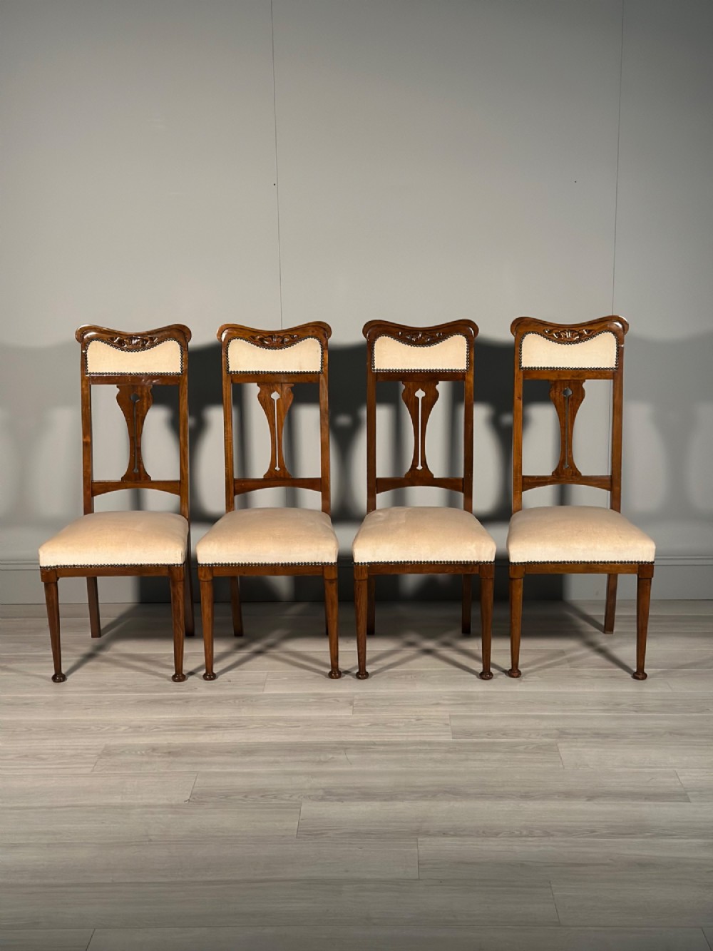 A set of four antique Biedermeier dining chairs featuring carved wooden frames, pierced back splats, and cream upholstered seats with brass stud detailing.