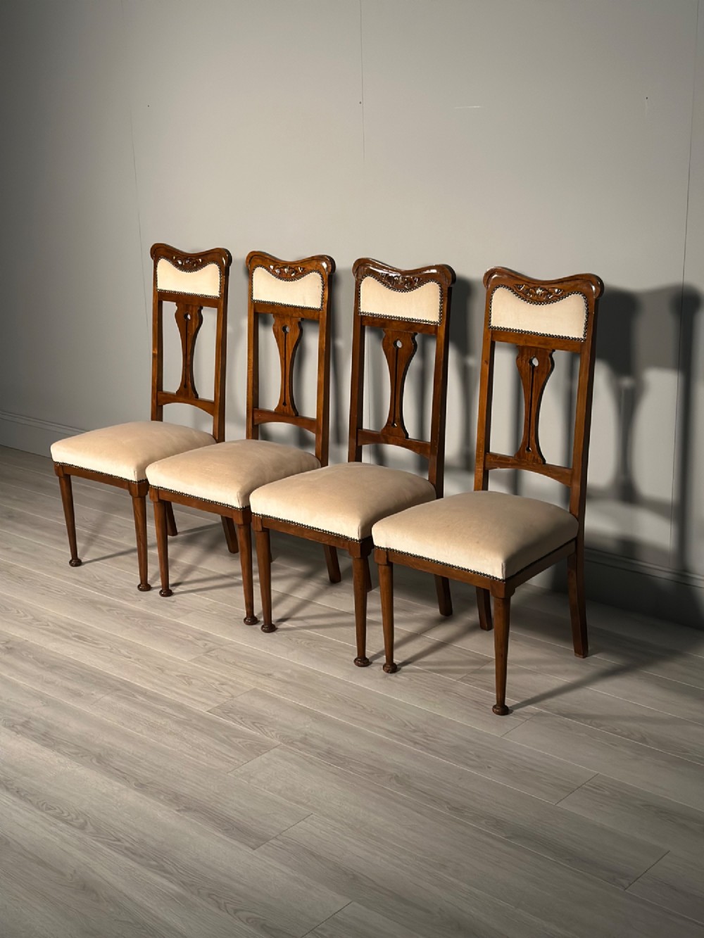 A set of four antique Biedermeier dining chairs featuring carved wooden frames, pierced back splats, and cream upholstered seats with brass stud detailing. View II