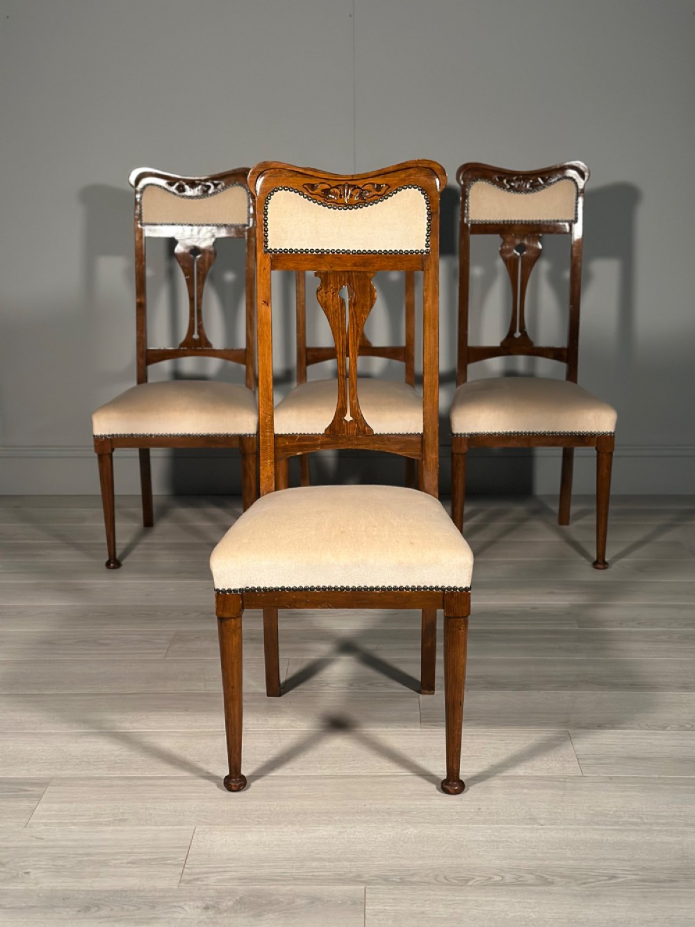 A set of four antique Biedermeier dining chairs featuring carved wooden frames, pierced back splats, and cream upholstered seats with brass stud detailing. View III