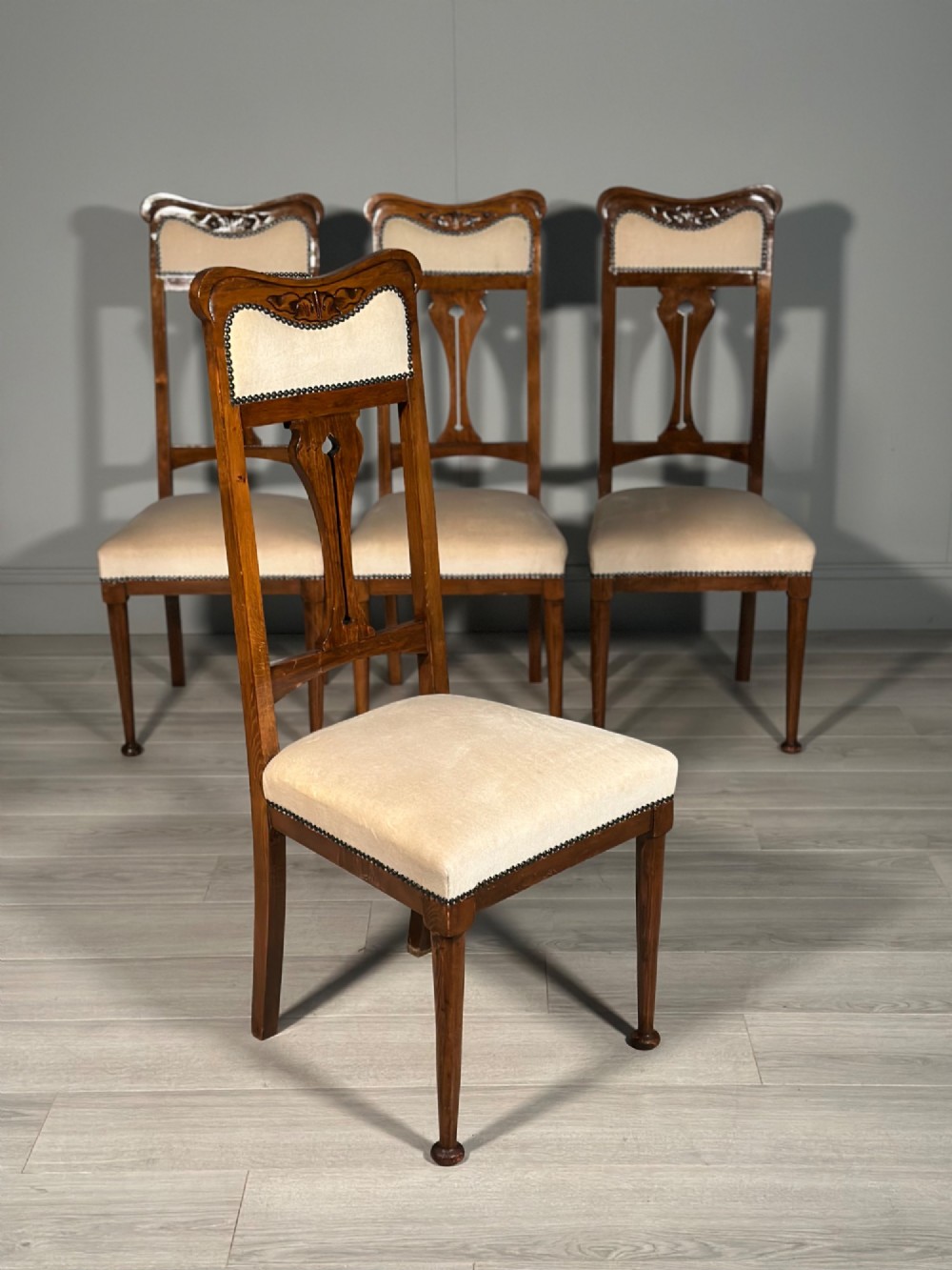 A set of four antique Biedermeier dining chairs featuring carved wooden frames, pierced back splats, and cream upholstered seats with brass stud detailing. View IV