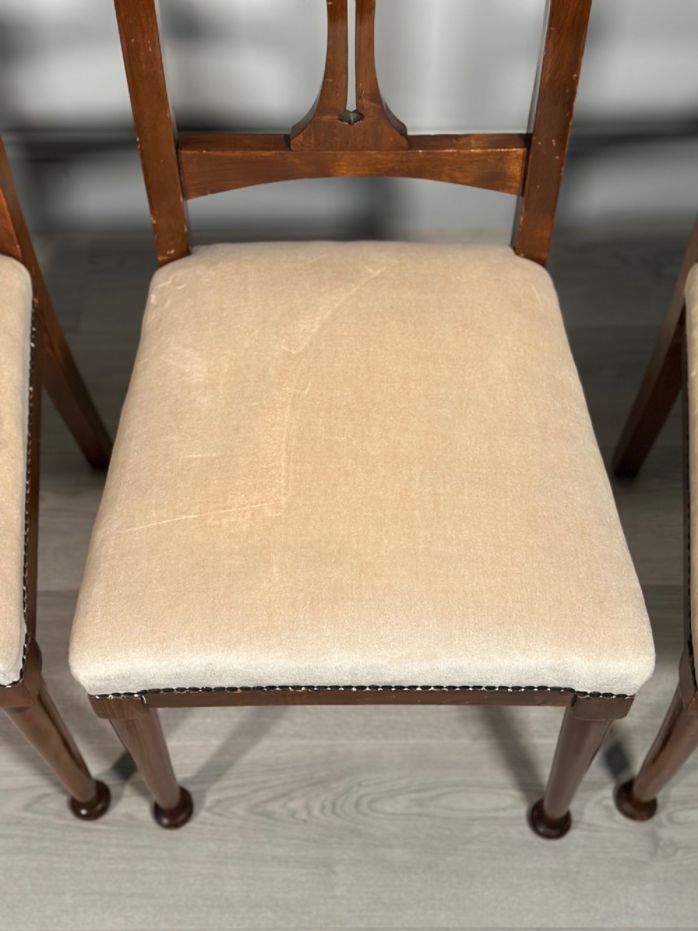 A set of four antique Biedermeier dining chairs featuring carved wooden frames, pierced back splats, and cream upholstered seats with brass stud detailing. View VI