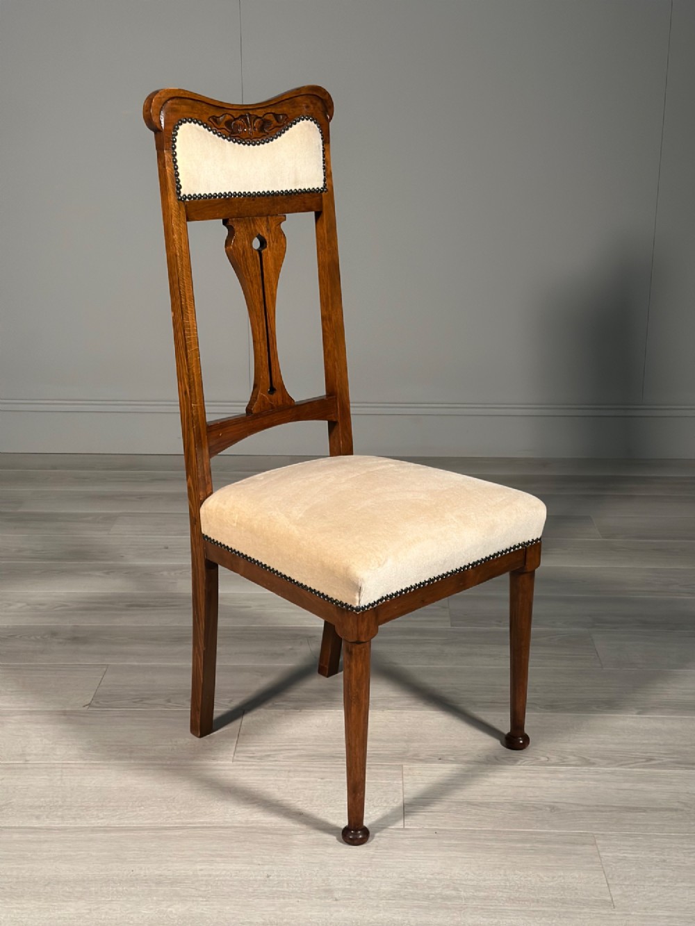 A set of four antique Biedermeier dining chairs featuring carved wooden frames, pierced back splats, and cream upholstered seats with brass stud detailing. View X