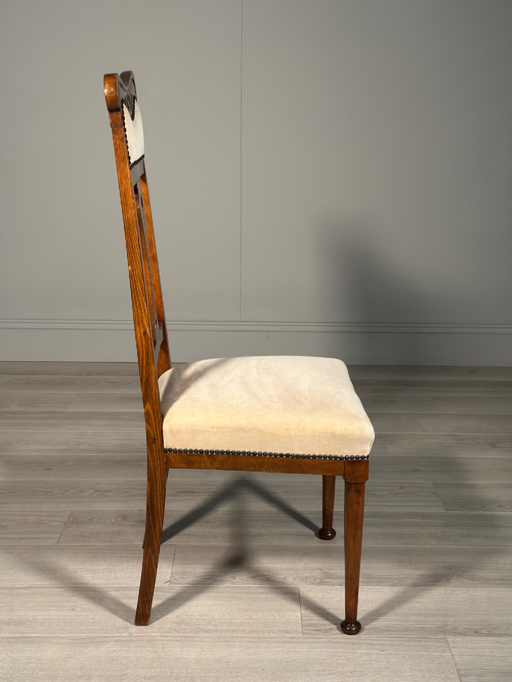 A set of four antique Biedermeier dining chairs featuring carved wooden frames, pierced back splats, and cream upholstered seats with brass stud detailing. View XV