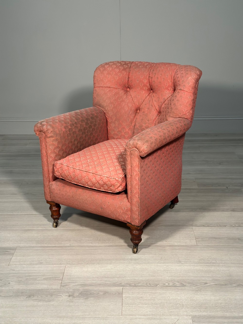 A Victorian button-back armchair upholstered in dusty pink patterned fabric with turned wooden front legs on brass castors.