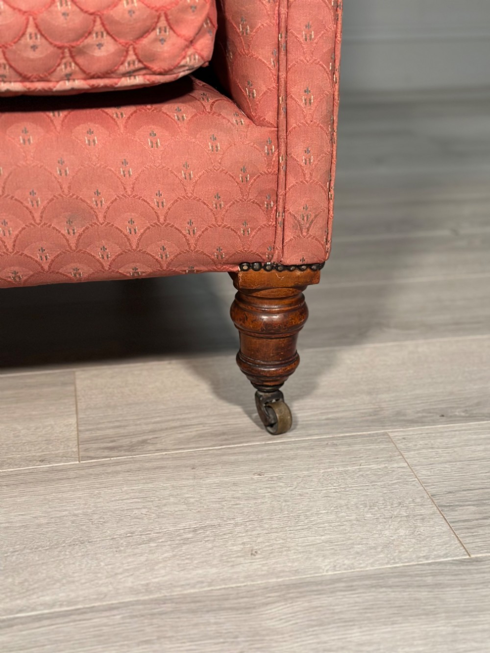 A Victorian button-back armchair upholstered in dusty pink patterned fabric with turned wooden front legs on brass castors. View III