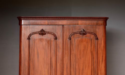 fig 1. A tall Victorian mahogany double wardrobe with twin panelled doors topped by carved arch mouldings and supported on a plinth base.