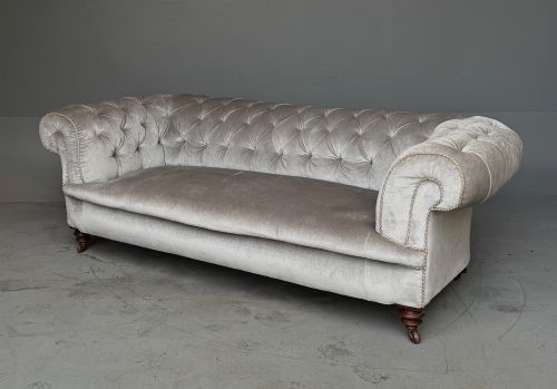 fig 1. A grey velvet Victorian Chesterfield sofa featuring deep-buttoned upholstery, low rolled arms, stud trim, and turned wood legs with brass casters.