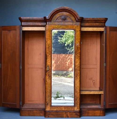 fig 1. A Victorian burr walnut triple wardrobe featuring an arched central mirrored door flanked by two panelled timber doors with carved mouldings.