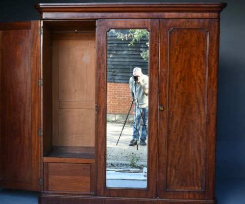 fig 1. A Victorian mahogany triple wardrobe featuring two outer panelled doors, a central mirrored door, and a moulded cornice top.