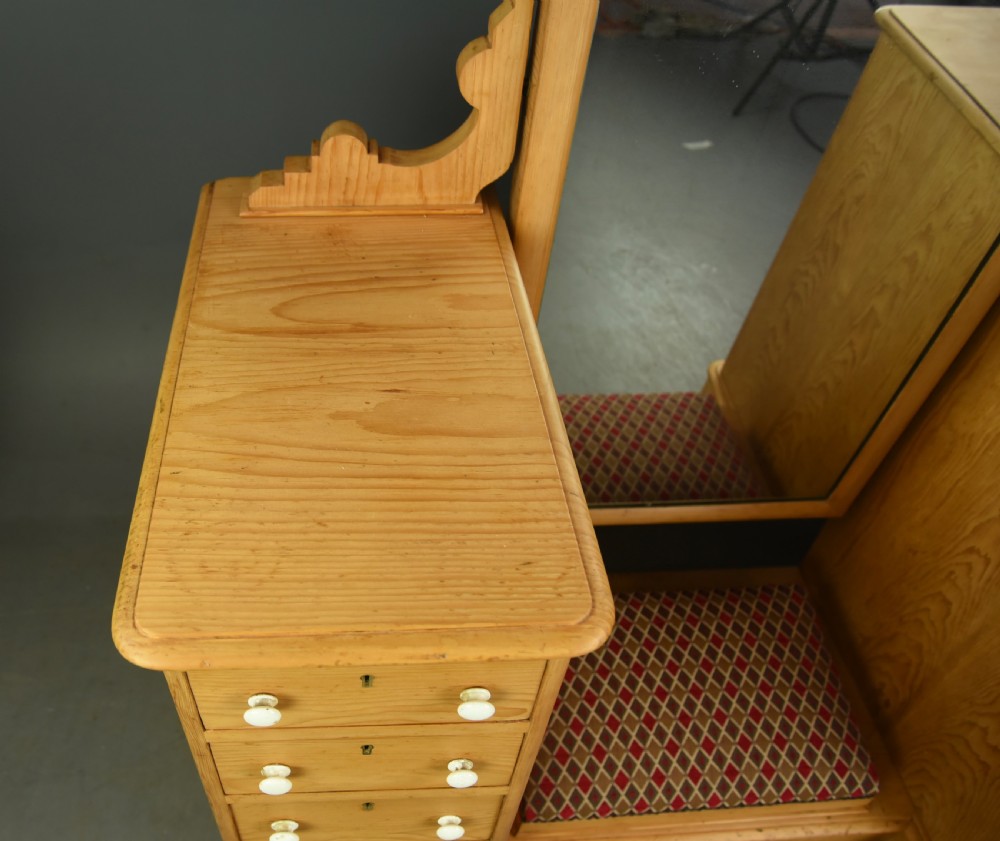 An antique Victorian pine dressing table featuring twin pedestals of five drawers each with white ceramic knobs, flanking a tall central arch-topped mirror and an upholstered footrest. View III