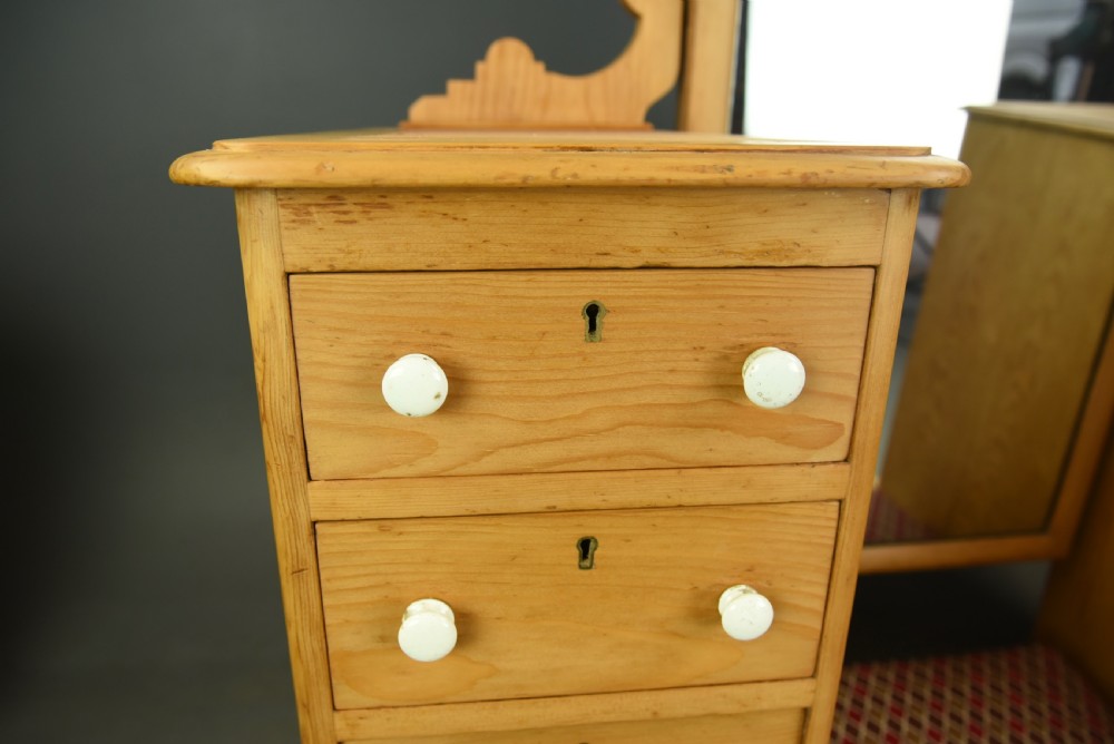 An antique Victorian pine dressing table featuring twin pedestals of five drawers each with white ceramic knobs, flanking a tall central arch-topped mirror and an upholstered footrest. View V