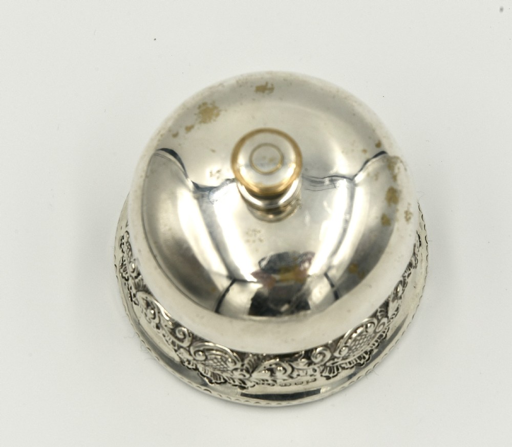 An antique sterling silver reception desk bell featuring a domed top plunger and a chased scroll base with British assay hallmarks. View II