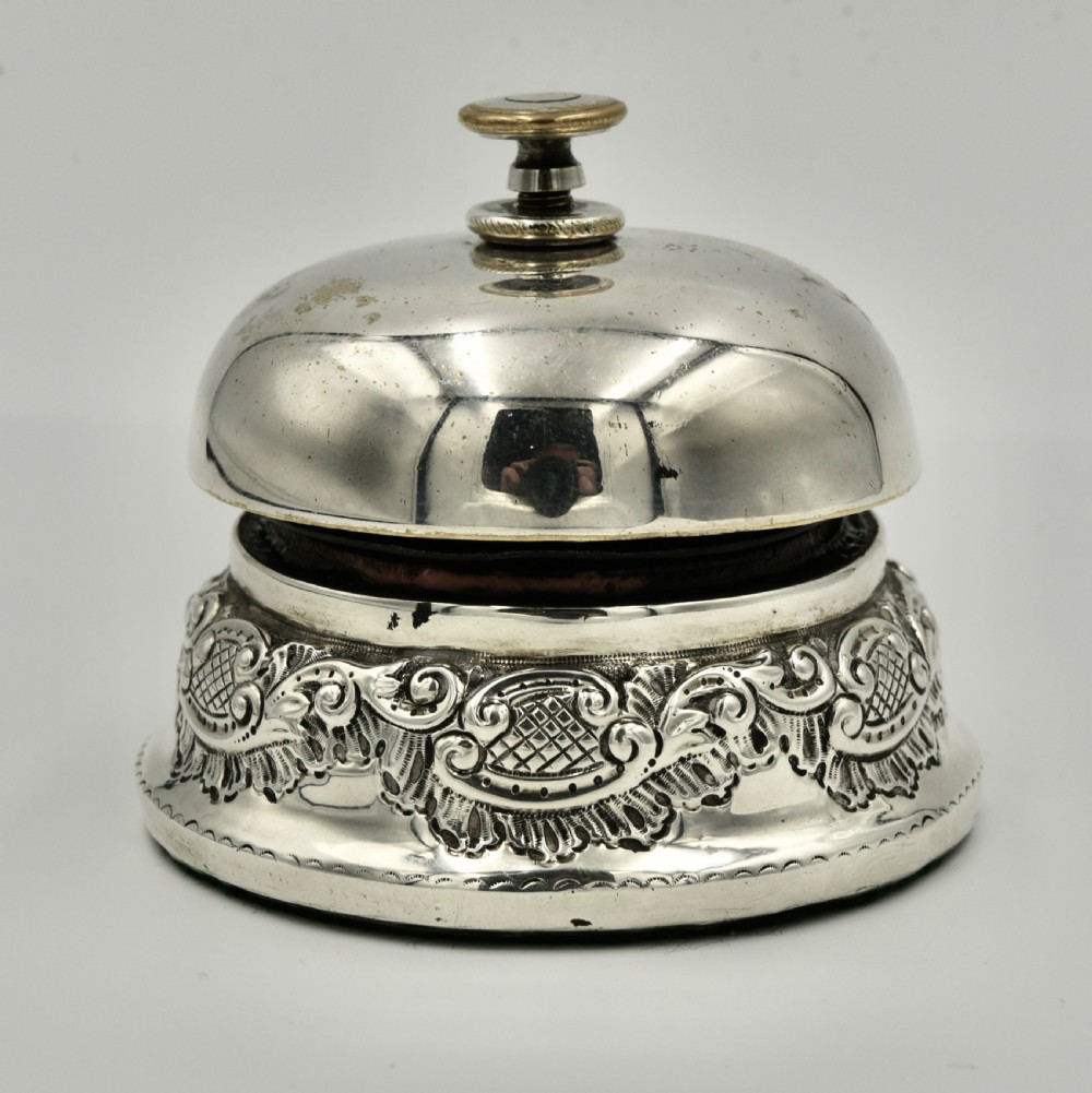 An antique sterling silver reception desk bell featuring a domed top plunger and a chased scroll base with British assay hallmarks. View III
