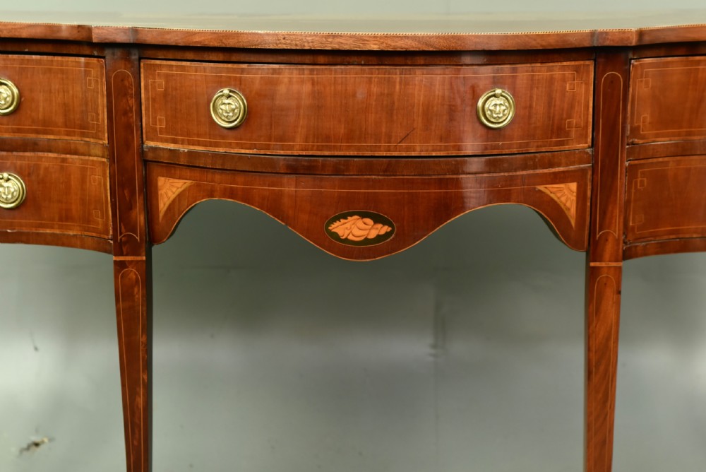 A Regency mahogany serpentine sideboard featuring curved drawer fronts, floral marquetry inlay, cast brass ring handles, and six tapered legs. View II