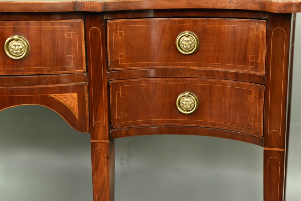 A Regency mahogany serpentine sideboard featuring curved drawer fronts, floral marquetry inlay, cast brass ring handles, and six tapered legs. View III